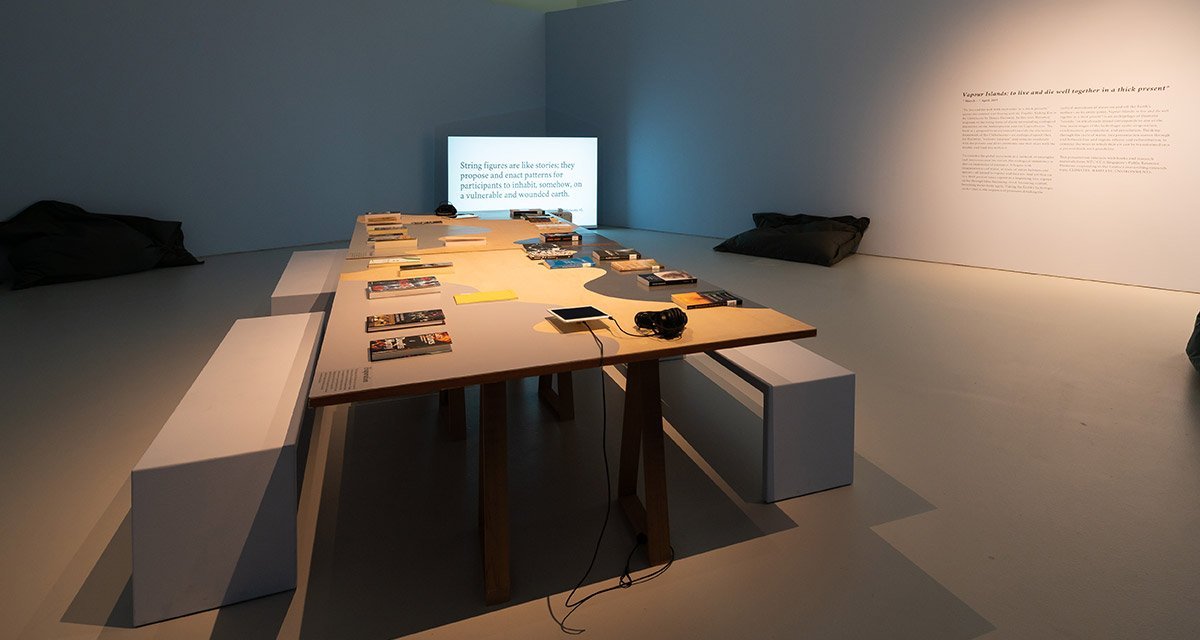 A table and a television screen inside a white room that displays research publications