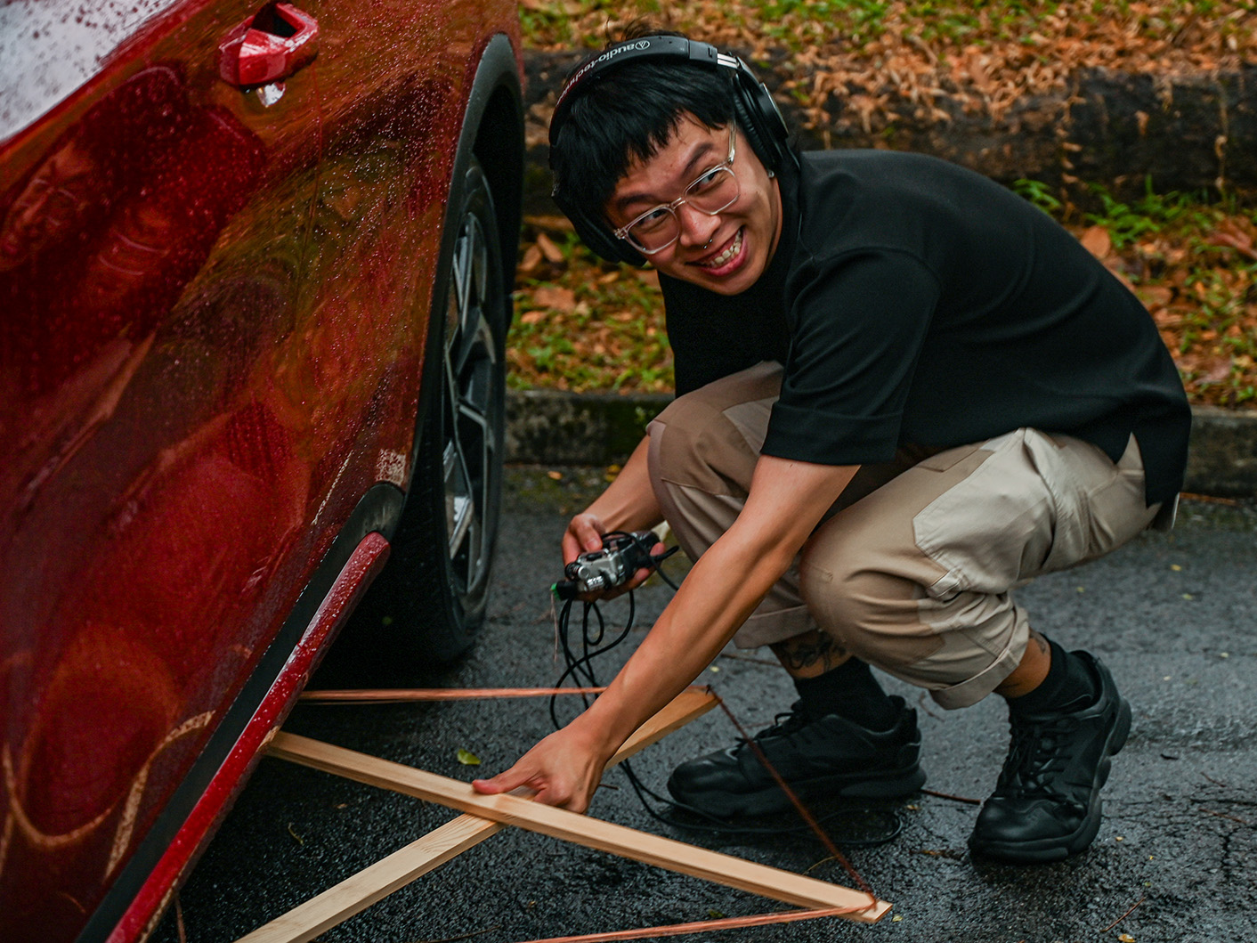 a man with a makeshift antenna listening to radio waves under a car